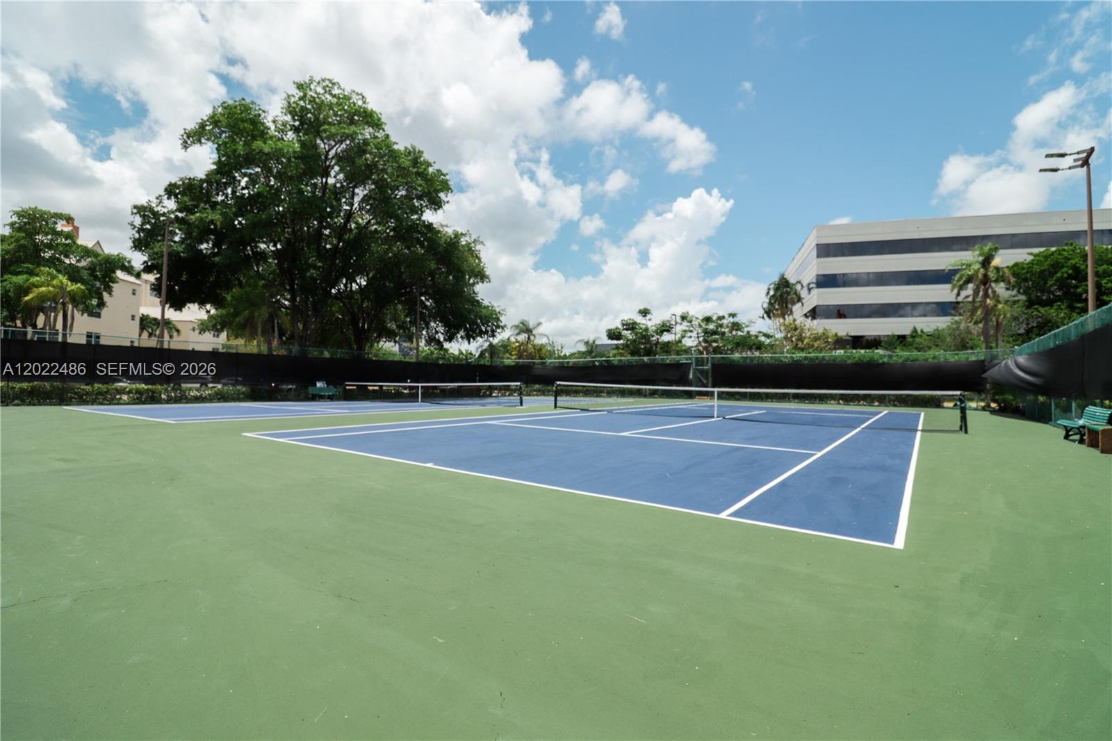 Two outdoor tennis courts with blue surfaces and green surrounding areas under a cloudy sky — 8245 Lake Dr # 308, Doral FL 33166, DORAL, FL