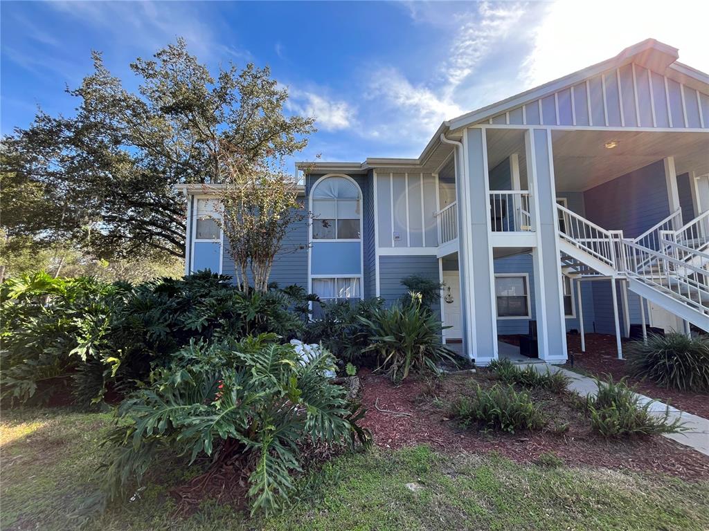A two-story blue apartment building features white trim, a staircase, and lush landscaping — 715 SUGAR BAY WAY UNIT 103, LAKE MARY, FL