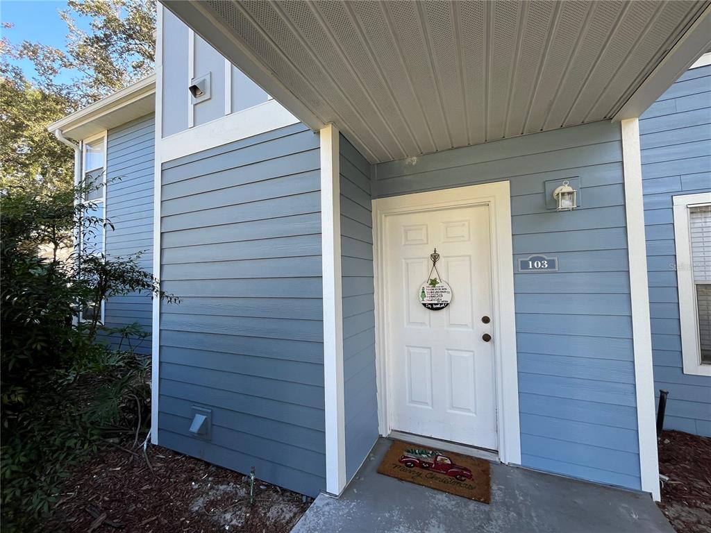 The exterior of a blue-sided building features a white front door labeled 103 — 715 SUGAR BAY WAY UNIT 103, LAKE MARY, FL