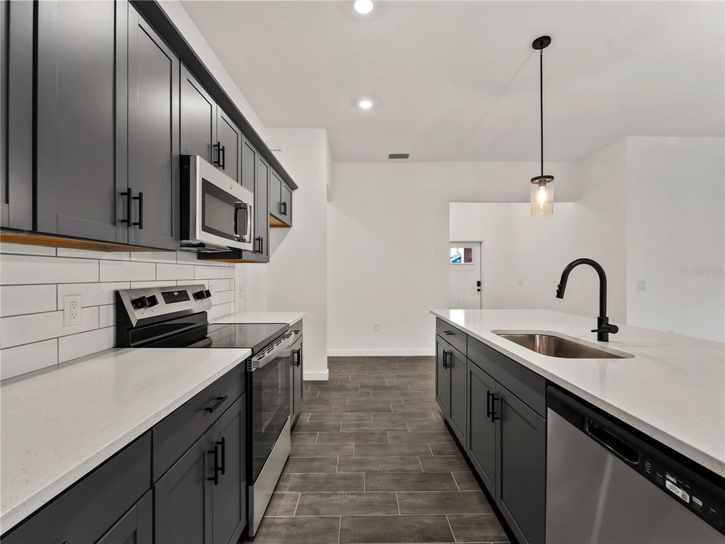 A modern kitchen features dark gray cabinets, white countertops, a center island, and tile flooring — 3855 LAMARQUE AVENUE, NORTH PORT, FL