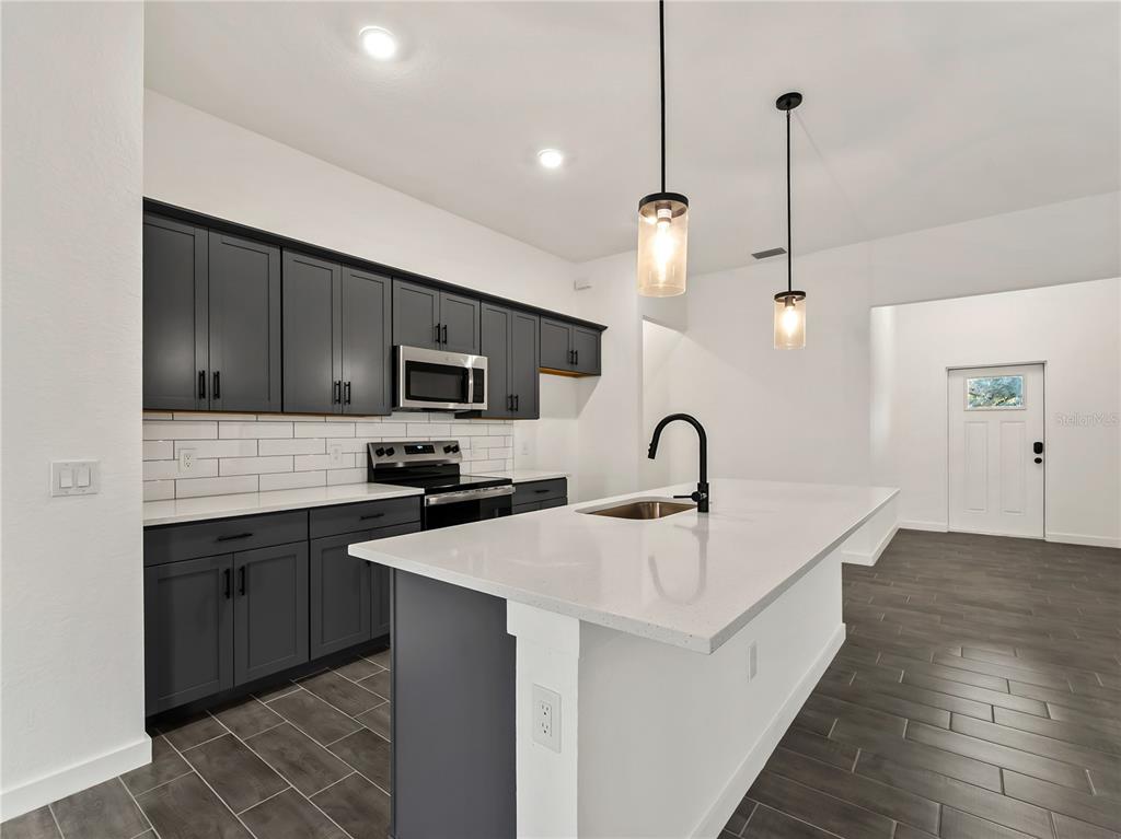 A modern kitchen features dark gray cabinets, white countertops, a center island, and tile flooring — 3855 LAMARQUE AVENUE, NORTH PORT, FL