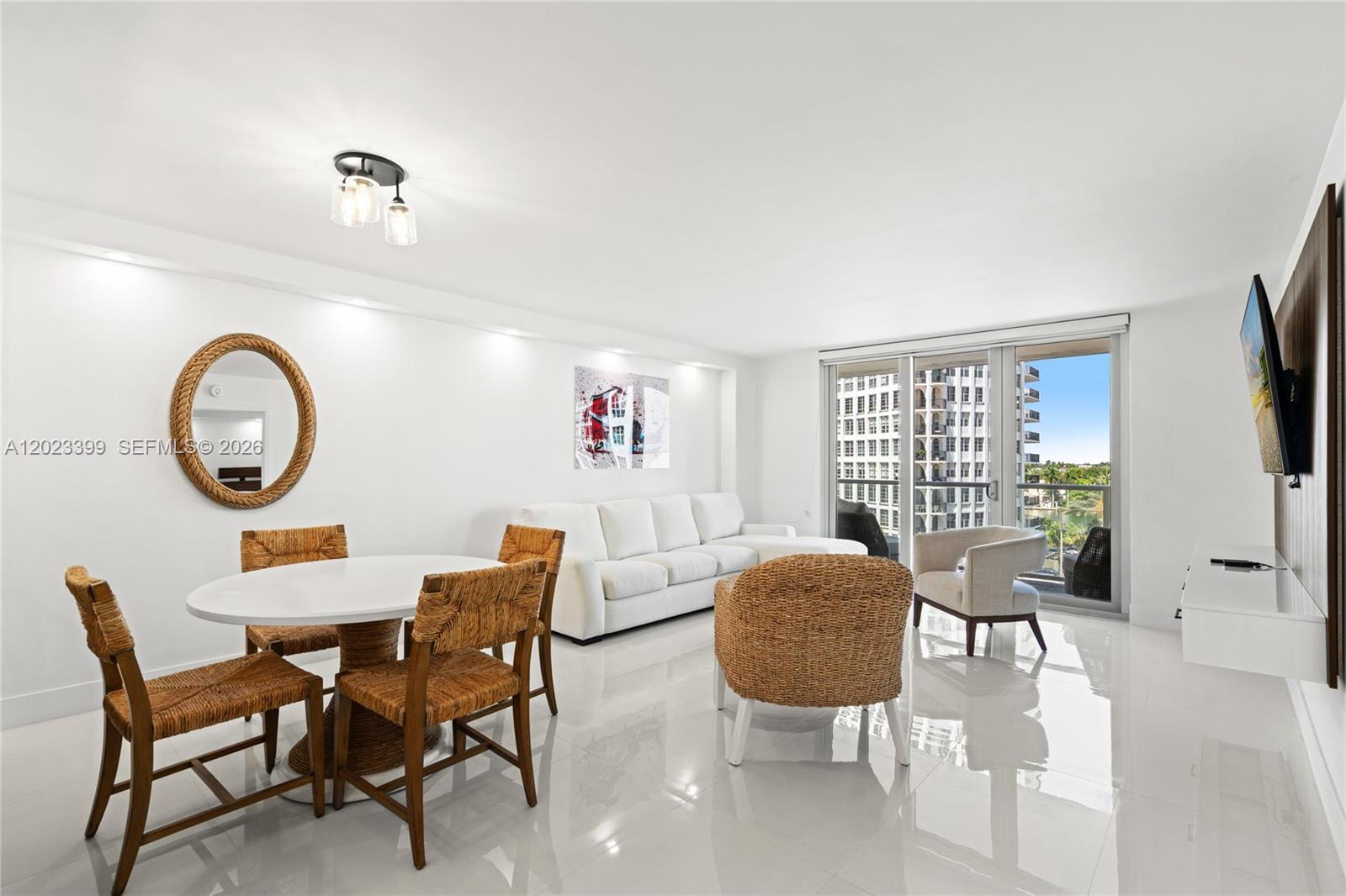 A bright living and dining area features white tile floors, wicker furniture, and balcony views — 5701 Collins Ave # 503, Miami Beach FL 33140, MIAMI BEACH, FL