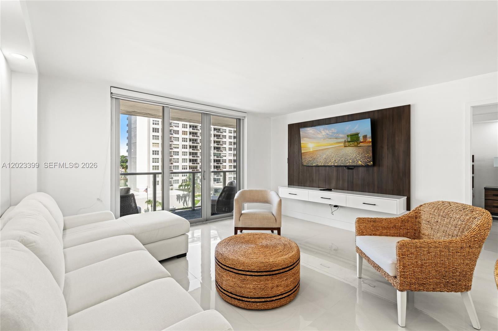 A living room features a white sectional sofa, a wicker chair, and a wall-mounted television — 5701 Collins Ave # 503, Miami Beach FL 33140, MIAMI BEACH, FL