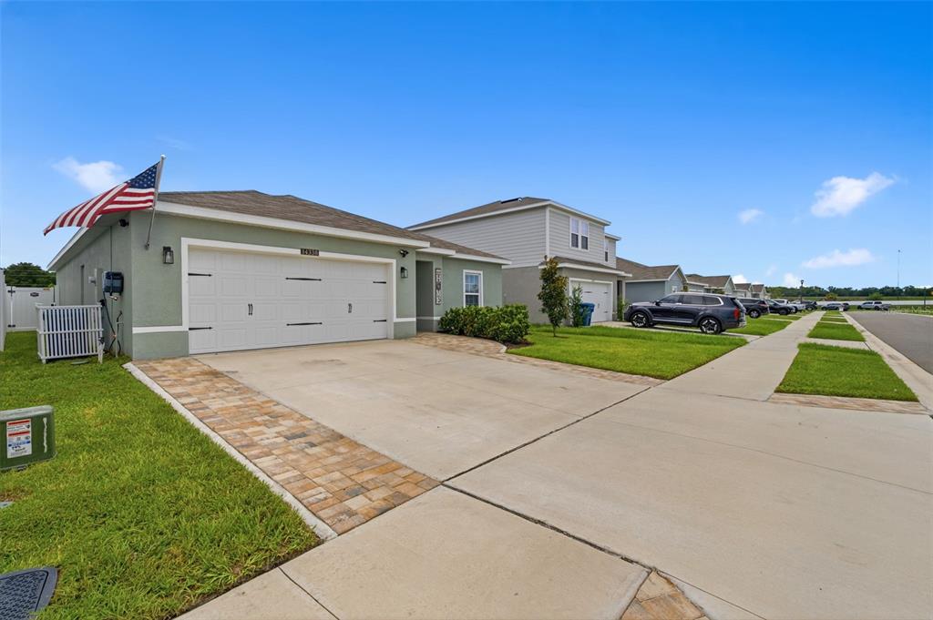A single-story house with a white garage door, brick-paved driveway, and an American flag — 14338 WHITEWATER WAY, BROOKSVILLE, FL