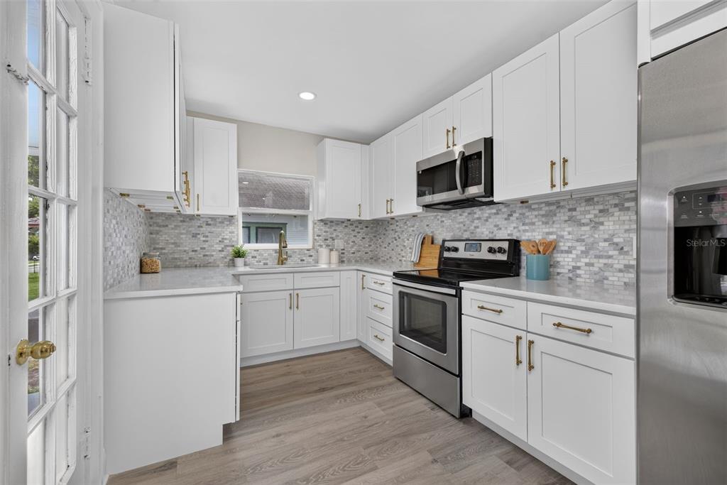 A modern kitchen features white cabinets, stainless steel appliances, a tiled backsplash, and wood-look flooring — 1201 OAKHILL STREET, LAKELAND, FL