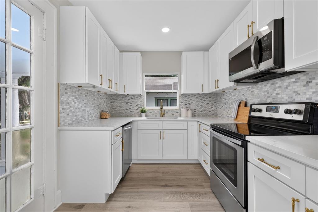 A kitchen with white cabinets, stainless steel appliances, quartz countertops, and a gray tiled backsplash — 1201 OAKHILL STREET, LAKELAND, FL