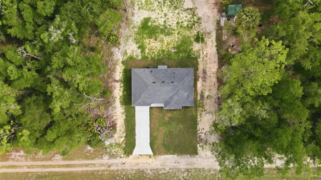 An aerial view shows a single-story house with a gray roof surrounded by wooded land — 9590 W TENNESSEE LANE, CRYSTAL RIVER, FL