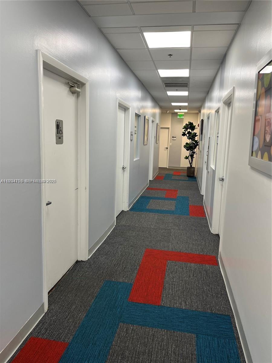 A hallway with gray walls, patterned carpet, and multiple white doors leads to a plant — 18191 NW 68th Ave, Miami FL 33015, MIAMI, FL