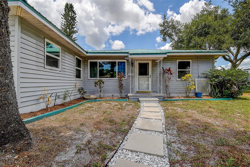 A single-story house with light gray siding, a green metal roof, and a stone walkway — 1509 CANTERBURY ROAD N, ST PETERSBURG, FL