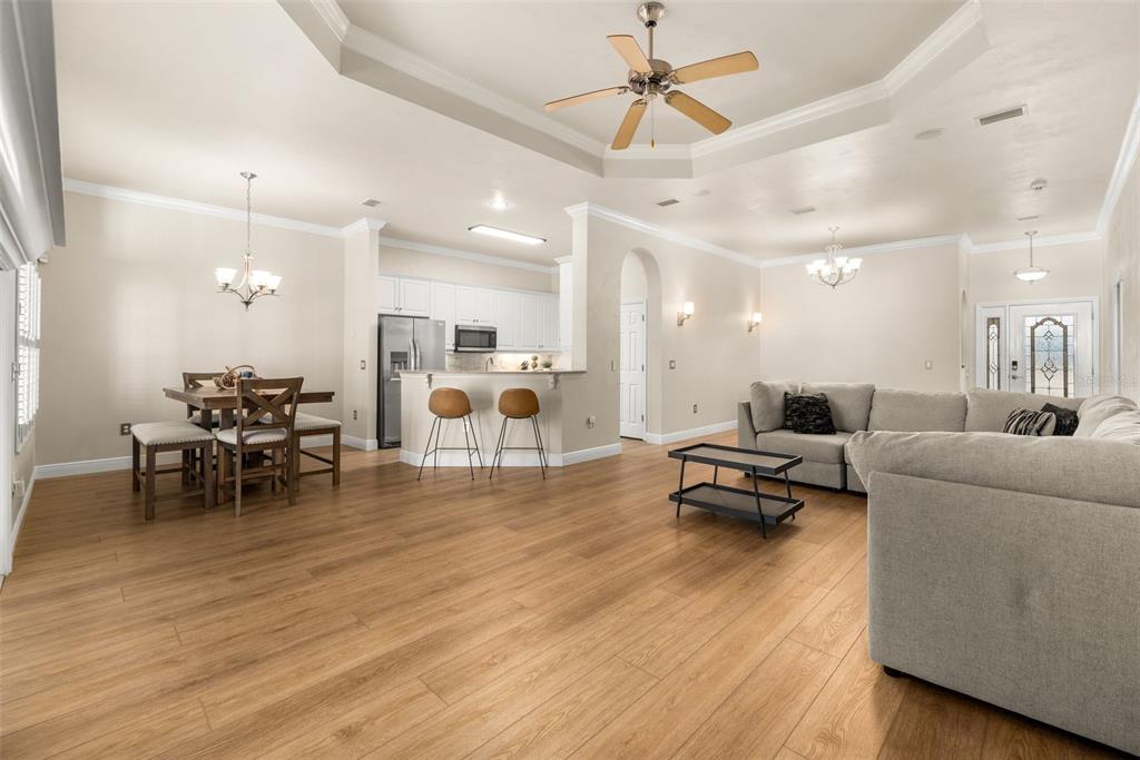 An open-concept living and dining area features light wood flooring, white cabinetry, and a tray ceiling — 3737 SW 74TH DRIVE, GAINESVILLE, FL