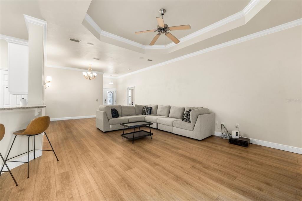 A living room features a light-colored sectional sofa, wood-look flooring, and a tray ceiling — 3737 SW 74TH DRIVE, GAINESVILLE, FL