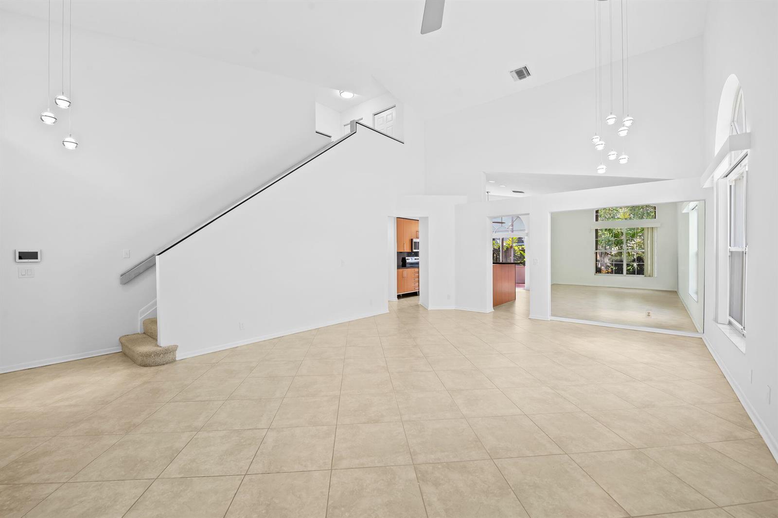 A spacious living room features white walls, tile flooring, a staircase, and a large mirror — 2712 Cayenne Avenue, Cooper City FL 33026, COOPER CITY, FL