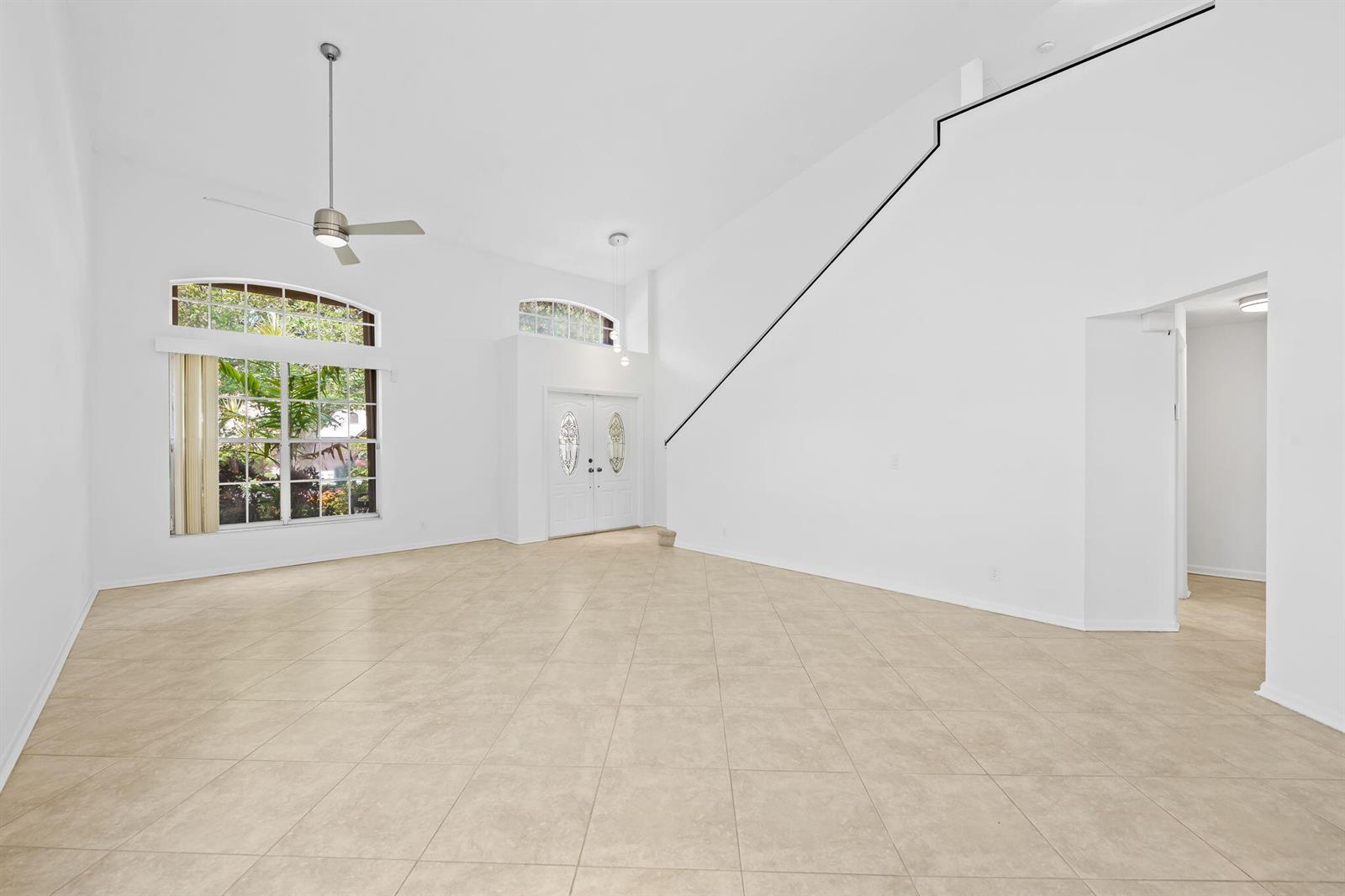 A spacious, empty living room with high ceilings, white walls, and light-colored tile flooring — 2712 Cayenne Avenue, Cooper City FL 33026, COOPER CITY, FL