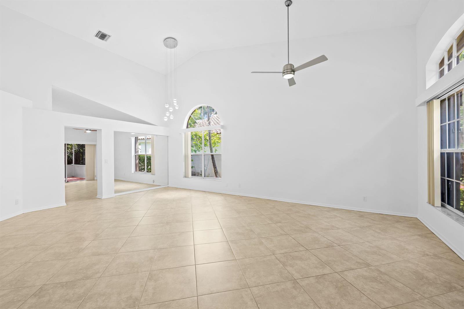 A bright, high-ceilinged living room features beige tile flooring, a ceiling fan, and large windows — 2712 Cayenne Avenue, Cooper City FL 33026, COOPER CITY, FL
