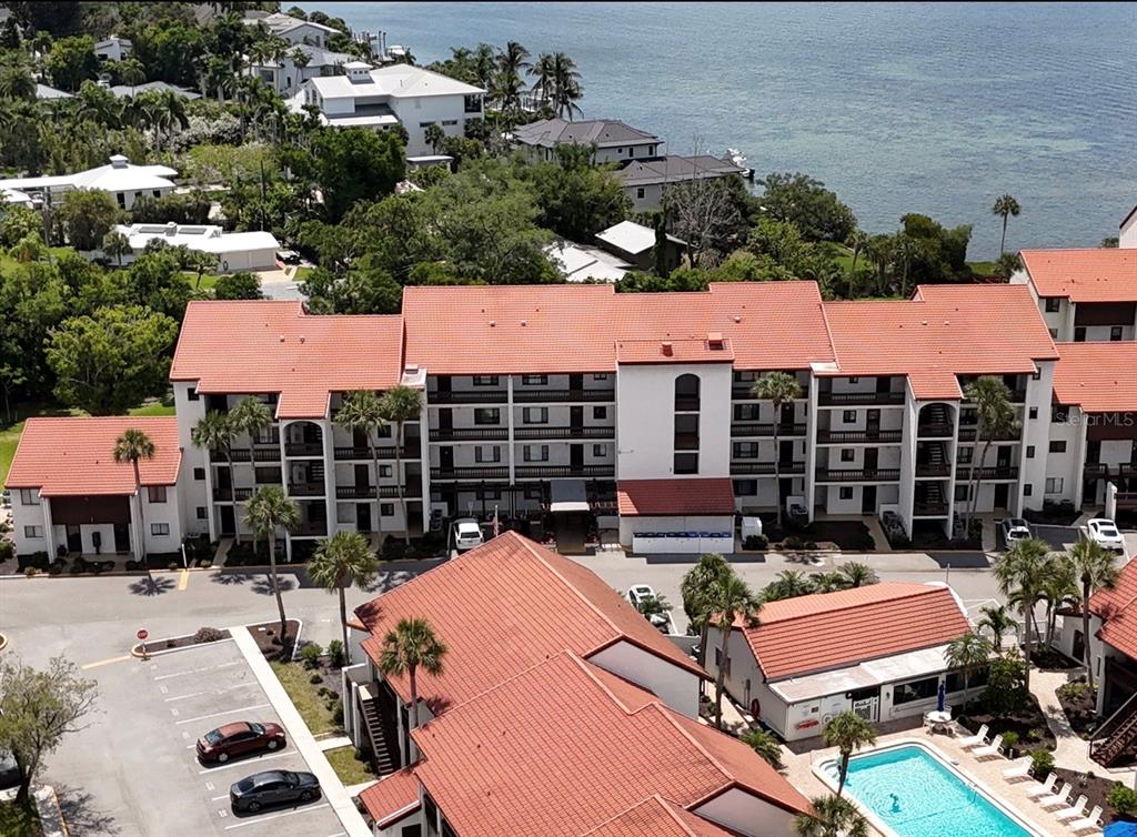 An aerial view shows a multi-story apartment complex with red tile roofs and a pool — 1624 STICKNEY POINT ROAD UNIT 206, SARASOTA, FL
