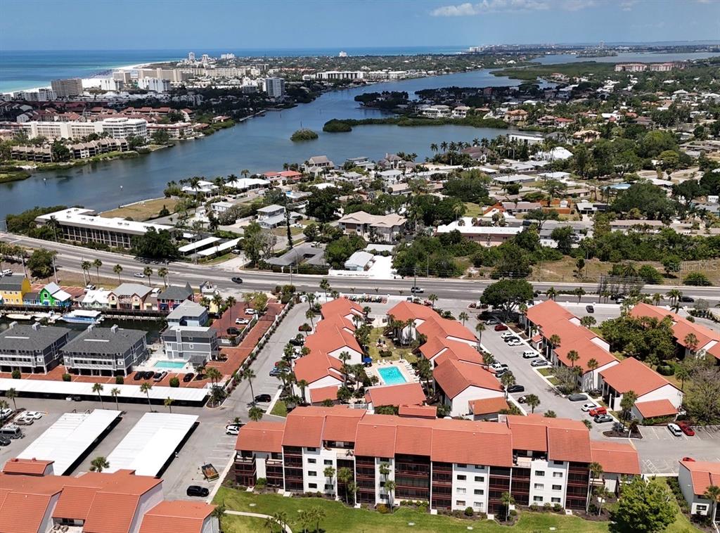 An aerial view shows a multi-story residential complex with red-tiled roofs near a waterway — 1624 STICKNEY POINT ROAD UNIT 206, SARASOTA, FL