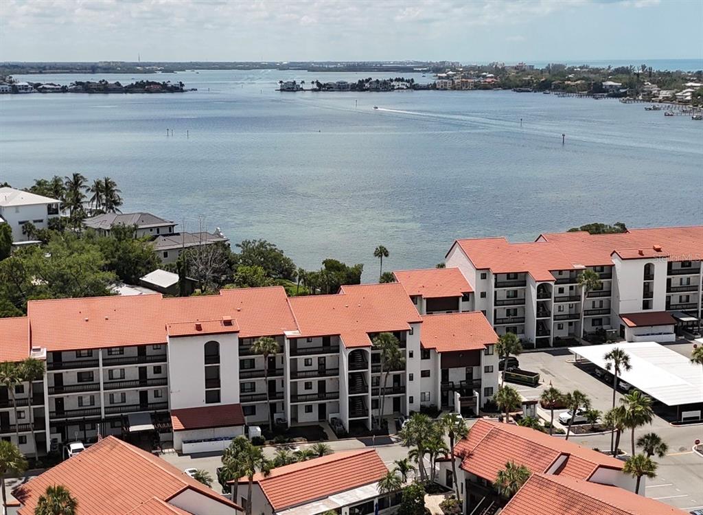 An aerial view shows multi-story apartment buildings with red tile roofs overlooking a large bay — 1624 STICKNEY POINT ROAD UNIT 206, SARASOTA, FL