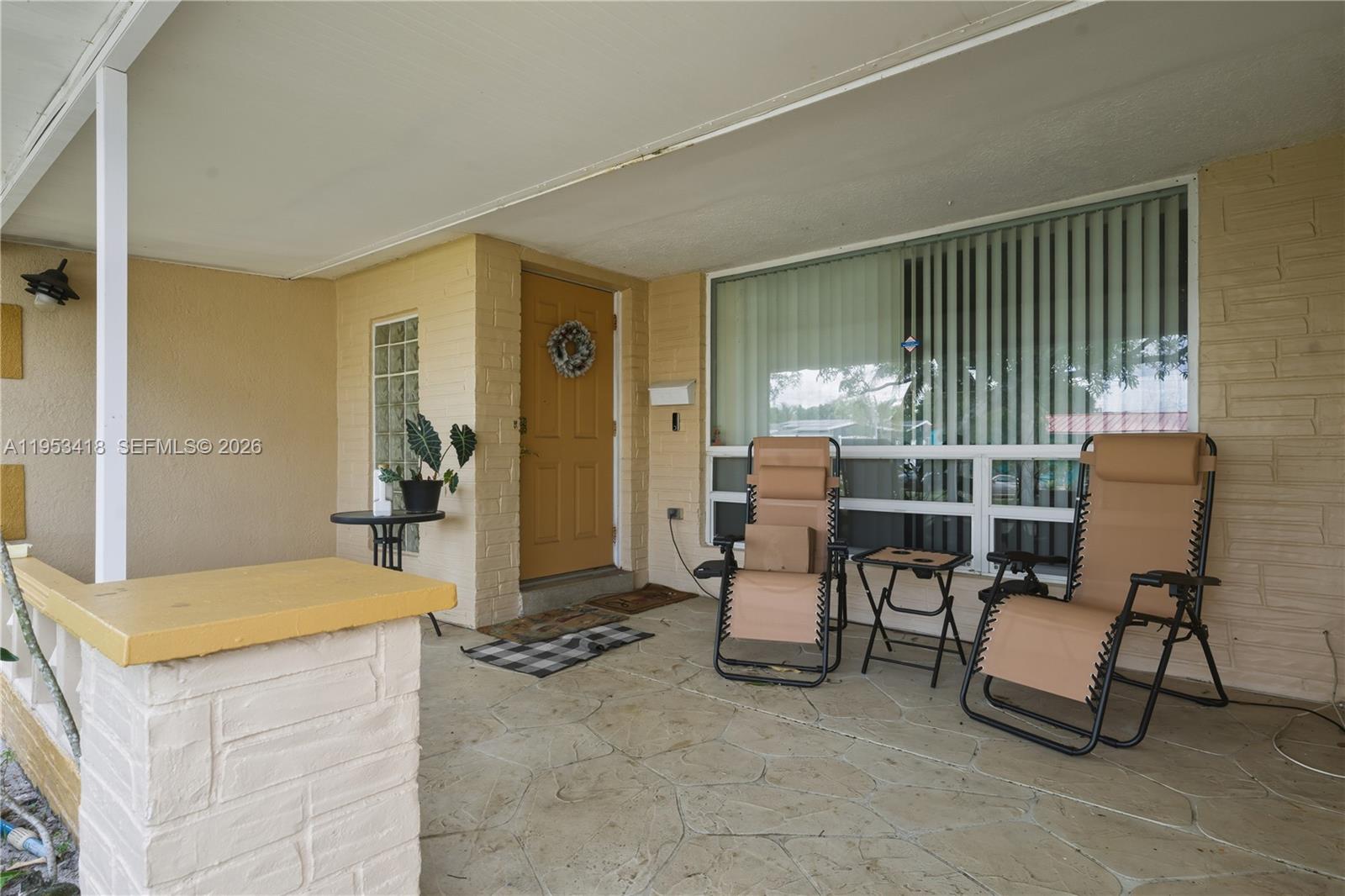 A covered front porch features a brick wall, a yellow door, and two lounge chairs — 7630 Embassy Blvd, Miramar FL 33023, MIRAMAR, FL