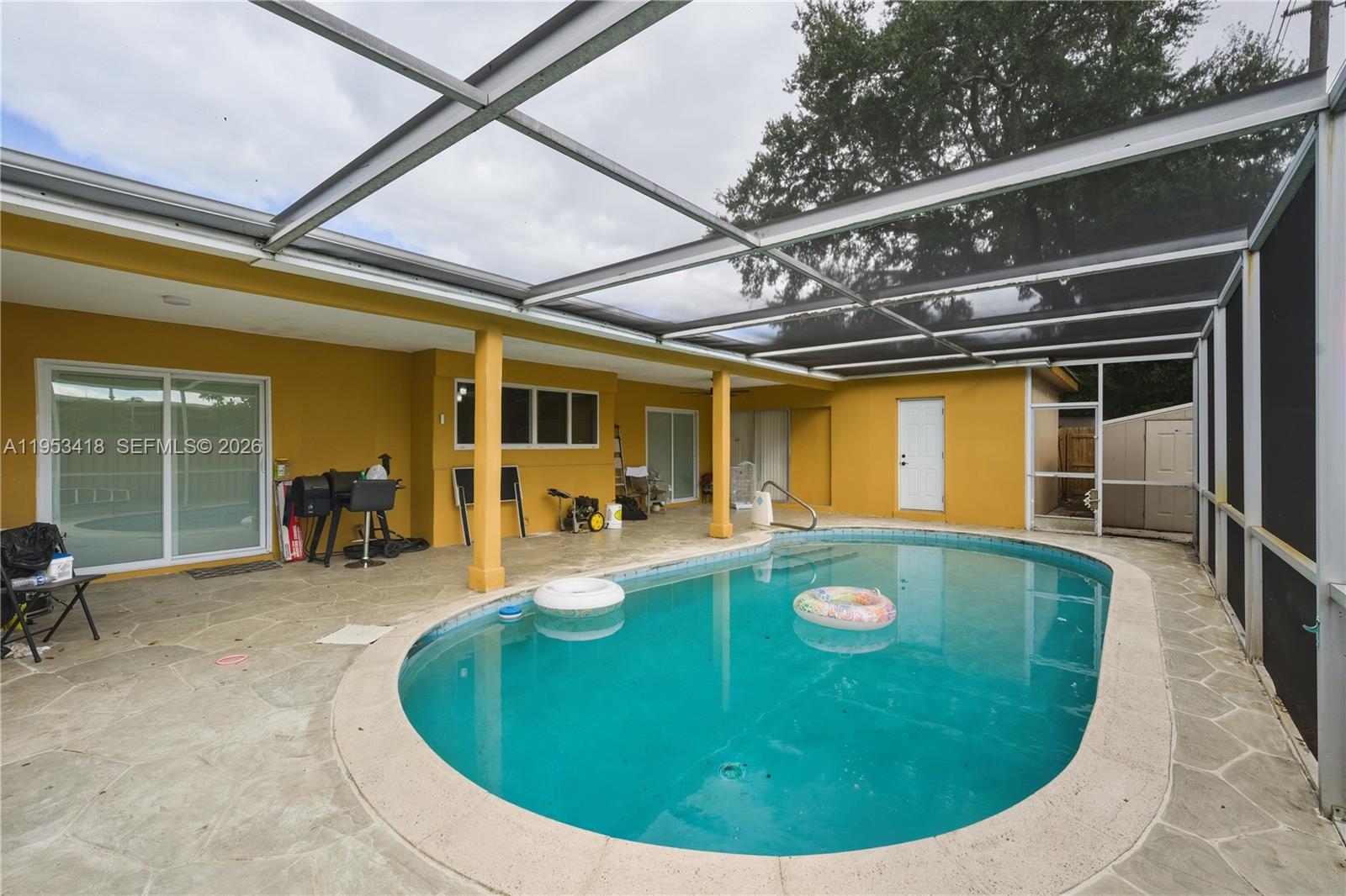 A screened-in patio features a swimming pool, yellow exterior walls, and stone-patterned flooring — 7630 Embassy Blvd, Miramar FL 33023, MIRAMAR, FL