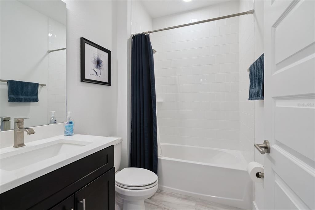 A bathroom features a dark vanity, white countertop, toilet, and a tub with white tile — 14014 SCARLET ASTER ALLEY, WINTER GARDEN, FL