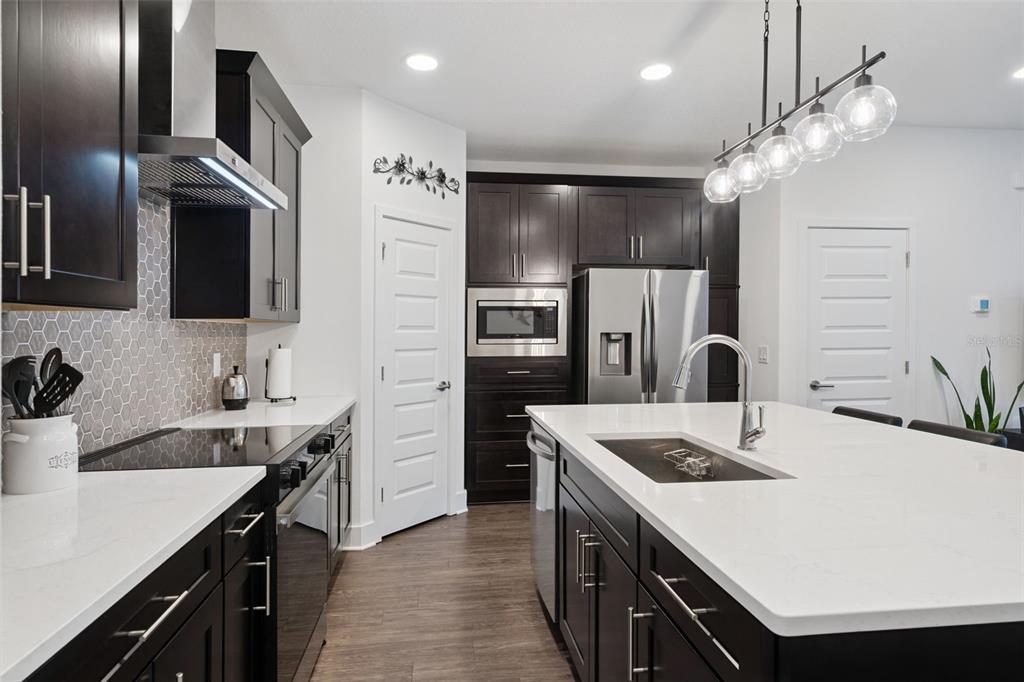 A modern kitchen features dark wood cabinets, white countertops, a central island, and stainless appliances — 14014 SCARLET ASTER ALLEY, WINTER GARDEN, FL