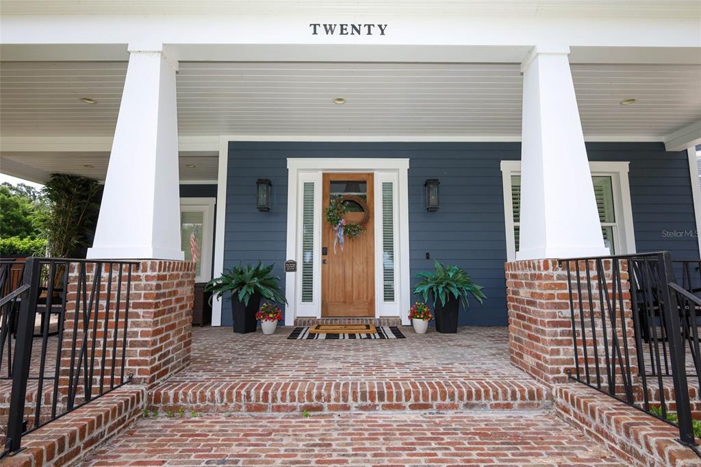 A front porch with brick flooring, white columns, and a blue-sided house entrance — 20 W CREST AVENUE, WINTER GARDEN, FL