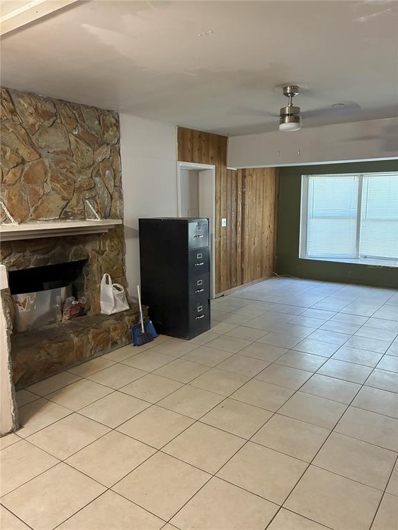 This room features a stone fireplace, tile flooring, wood-paneled walls, and a ceiling fan — 3016 BLOOMINGDALE AVENUE, VALRICO, FL