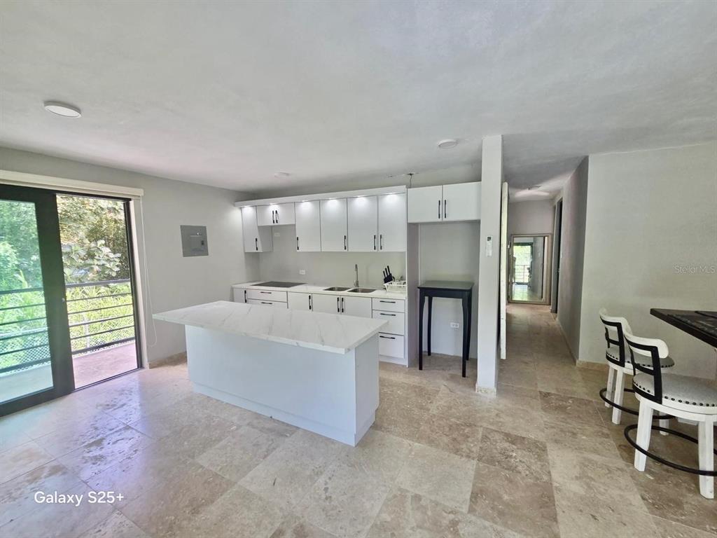 A modern kitchen features white cabinets, a marble-topped island, and light stone tile flooring — Solar 2 BARRIO ZARZAL, RIO GRANDE, PR