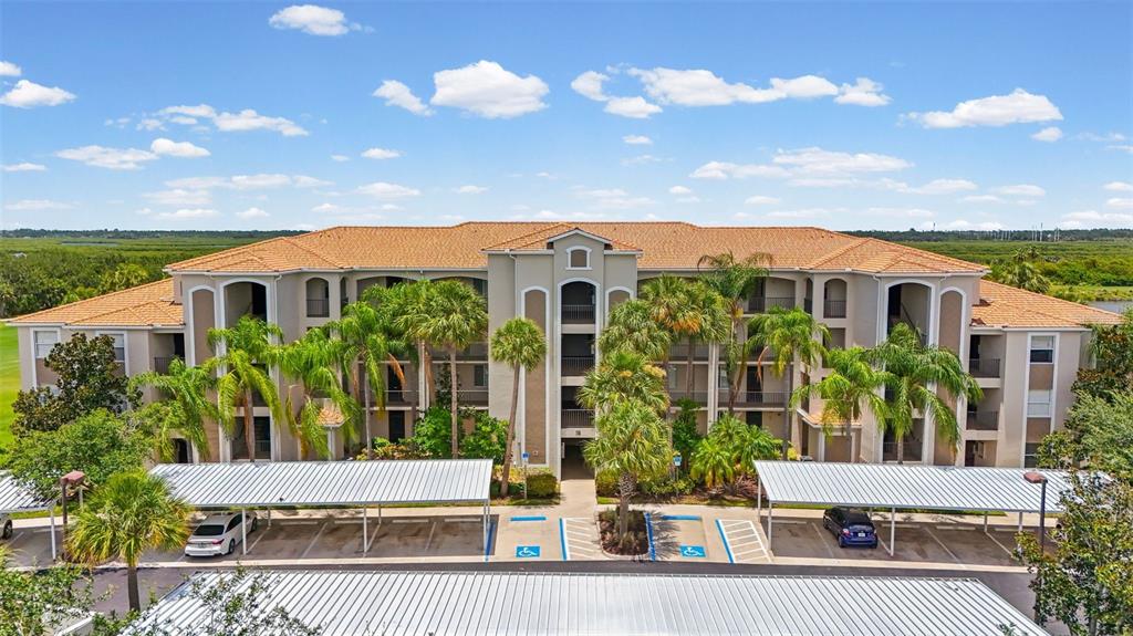 An aerial view of a multi-story apartment building with covered parking and a golf course — 7705 GRAND ESTUARY TRAIL UNIT 307, BRADENTON, FL