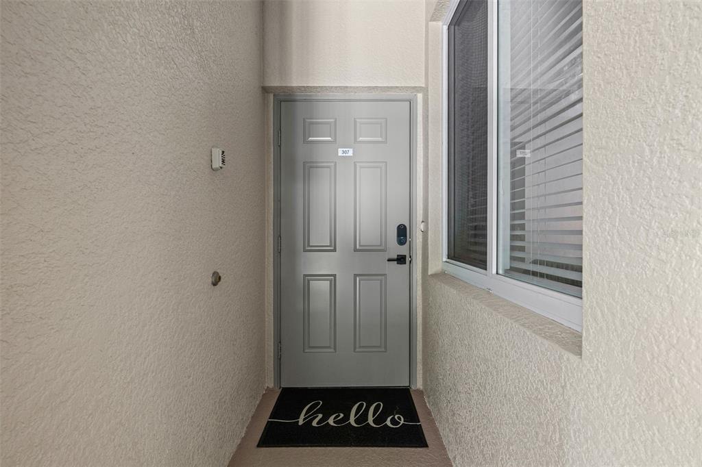 A hallway with wood-look flooring leads toward a living area with a brown sofa — 7705 GRAND ESTUARY TRAIL UNIT 307, BRADENTON, FL
