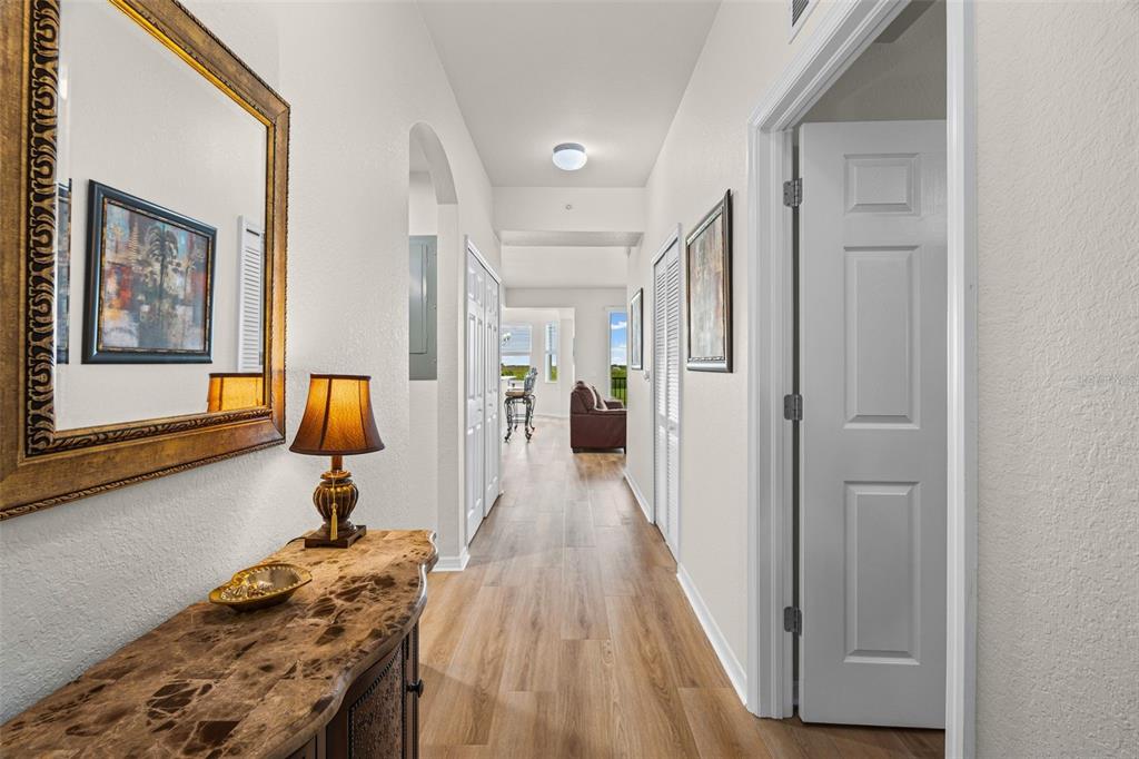 A hallway with light wood flooring leads to a white front door and two bedrooms — 7705 GRAND ESTUARY TRAIL UNIT 307, BRADENTON, FL