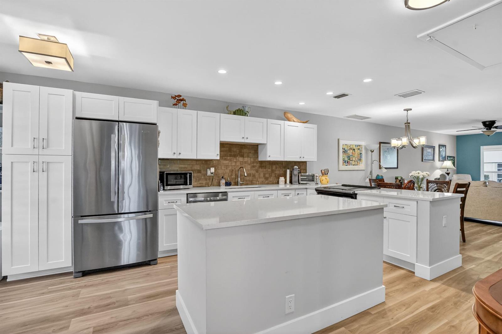 A kitchen features white cabinetry, stainless steel appliances, a central island, and light wood flooring — 8871 Warwick Drive, Boca Raton FL 33433, BOCA RATON, FL