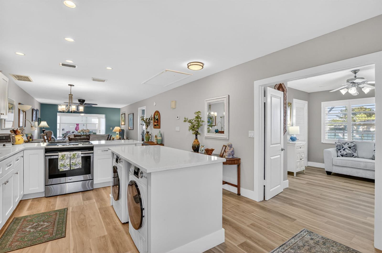 A kitchen with white cabinets, a quartz island containing laundry appliances, and light wood flooring — 8871 Warwick Drive, Boca Raton FL 33433, BOCA RATON, FL