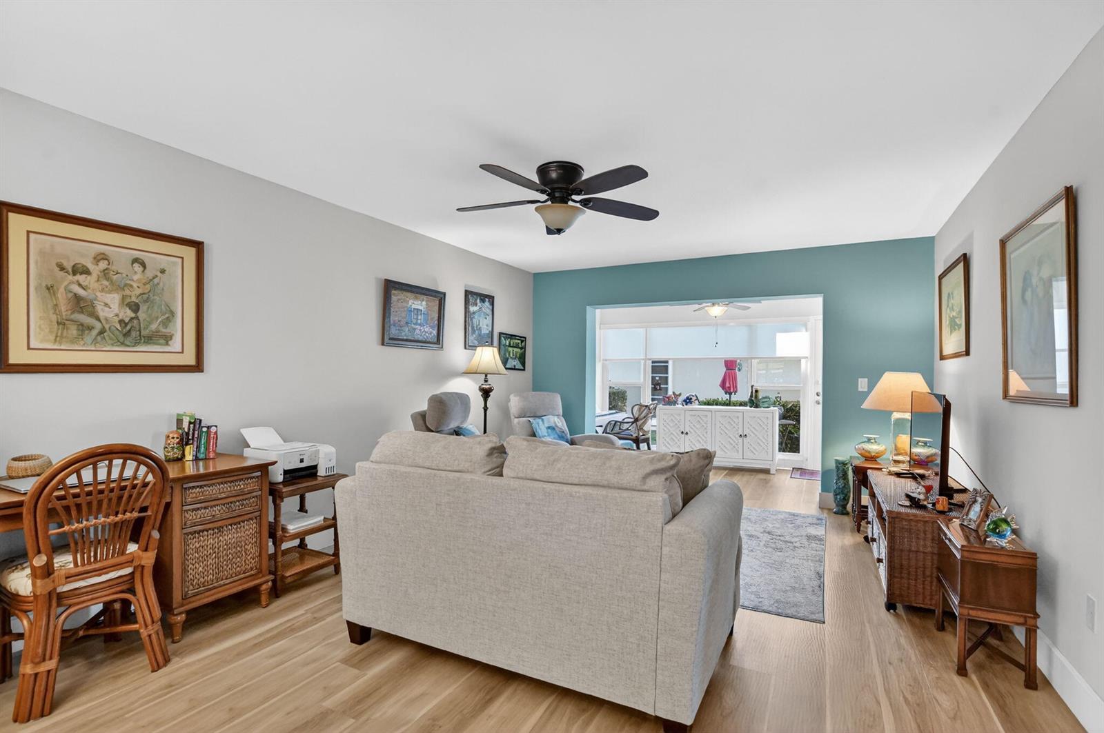 A living room with light wood flooring, a beige sofa, and a teal accent wall — 8871 Warwick Drive, Boca Raton FL 33433, BOCA RATON, FL