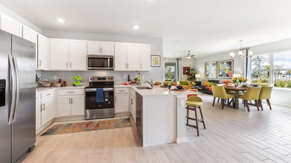 A modern kitchen with white cabinets and stainless steel appliances opens to a dining area — 4727 SCHUBERT TRAIL, NORTH PORT, FL