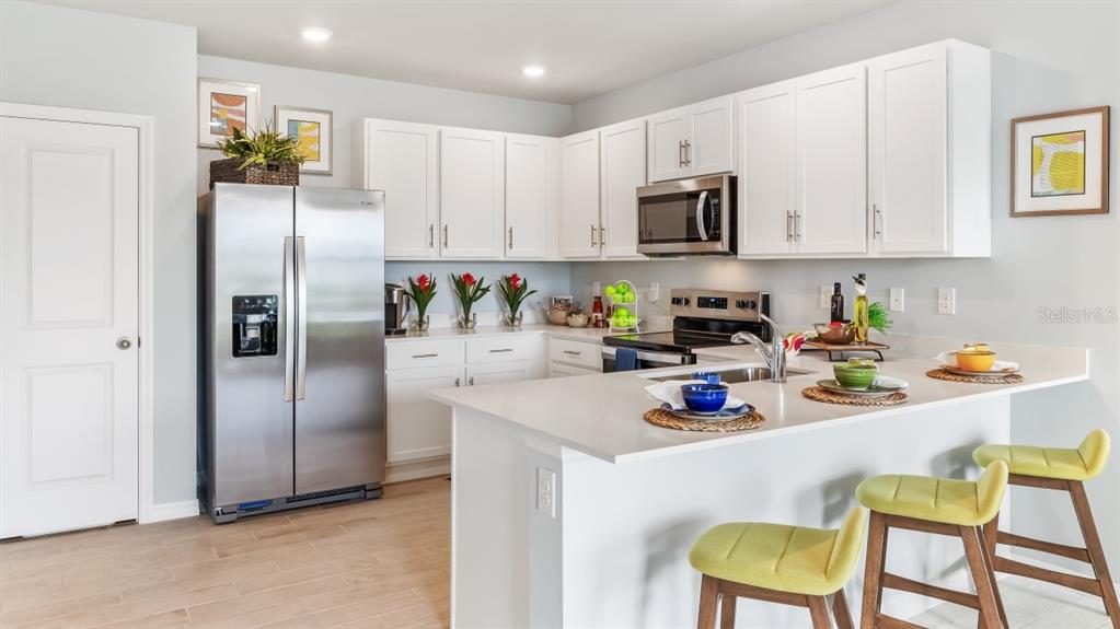 A modern kitchen features white cabinets, stainless steel appliances, and a quartz-topped island with stools — 4727 SCHUBERT TRAIL, NORTH PORT, FL