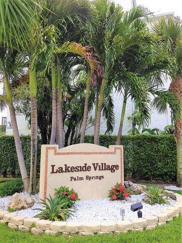 A stone sign for Lakeside Village Palm Springs sits in a landscaped garden with palms — 715 Lori Drive # 302, Palm Springs FL 33461, PALM SPRINGS, FL