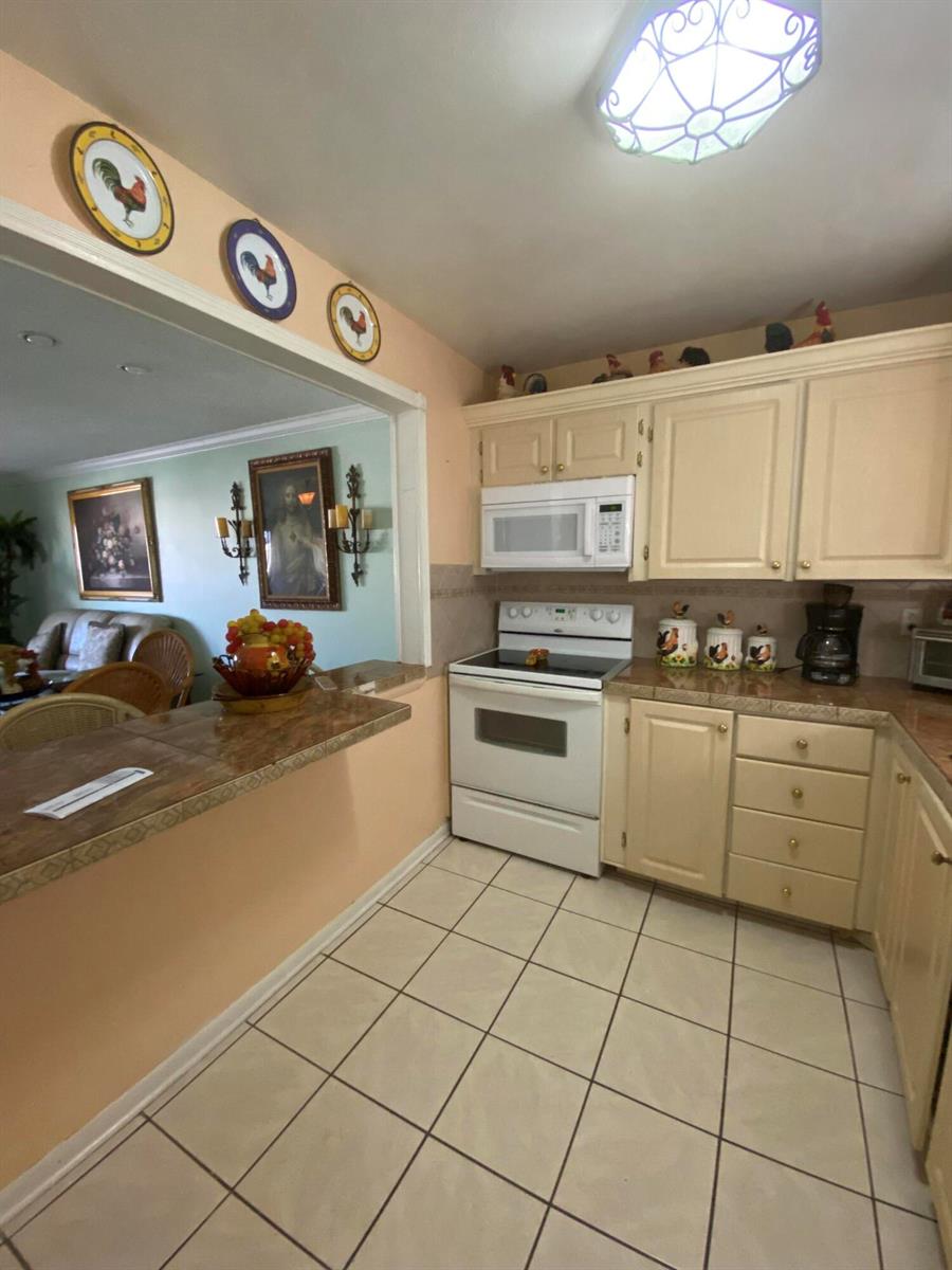 A kitchen with cream-colored cabinets, white appliances, and a tiled breakfast bar counter — 715 Lori Drive # 302, Palm Springs FL 33461, PALM SPRINGS, FL