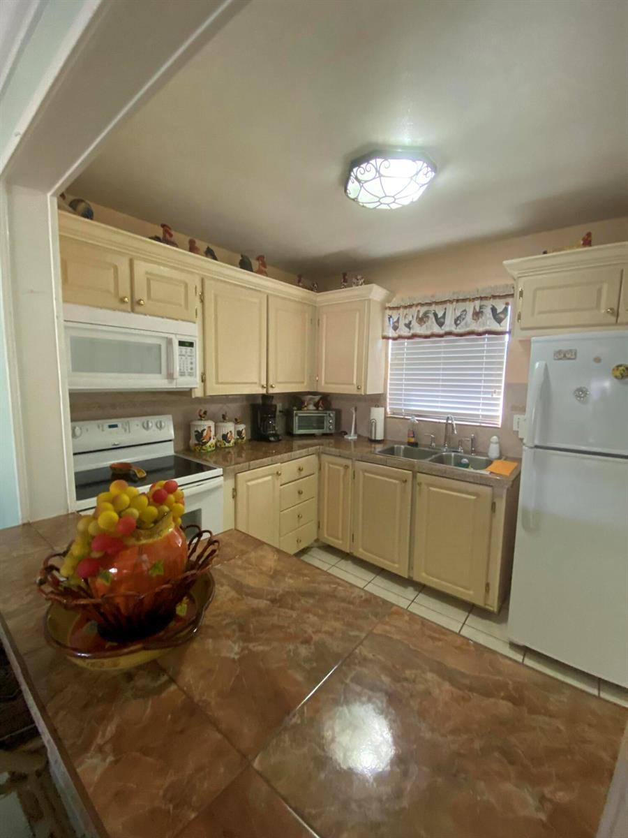 A kitchen features light-colored cabinets, a tiled countertop, and white appliances — 715 Lori Drive # 302, Palm Springs FL 33461, PALM SPRINGS, FL