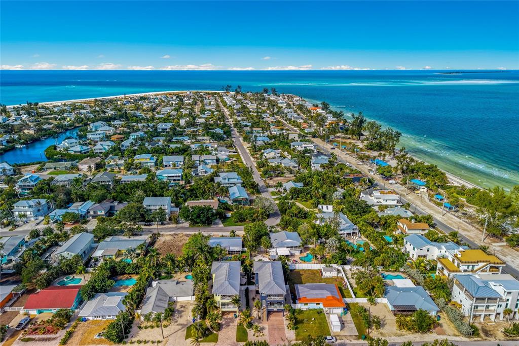 An aerial view shows a coastal neighborhood with houses, lush vegetation, and the ocean nearby — 159 CRESCENT DRIVE, ANNA MARIA, FL