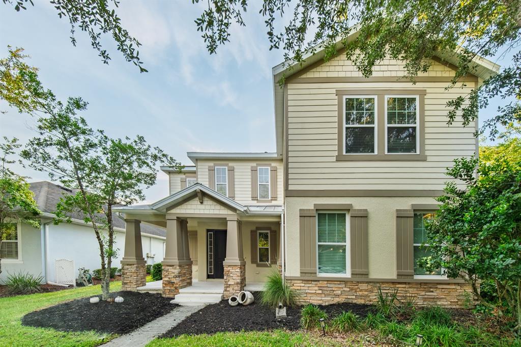 A two-story house with tan siding, stone accents, a covered front porch, and mature trees — 7912 HAMPTON LAKE DRIVE, TAMPA, FL