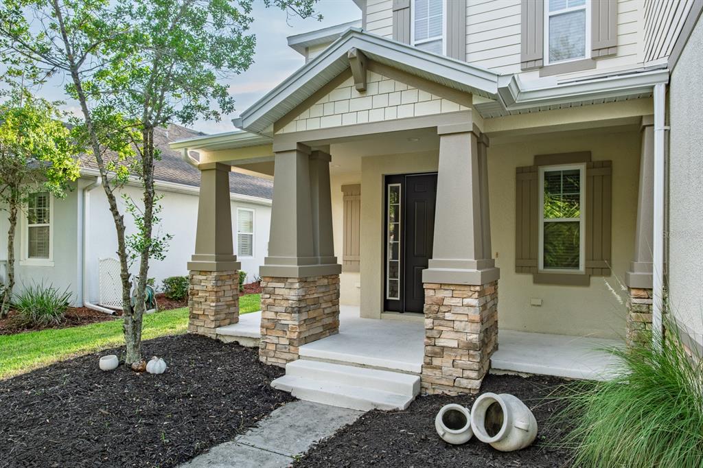 A front porch with stone-based columns and a dark door leads to a suburban home — 7912 HAMPTON LAKE DRIVE, TAMPA, FL