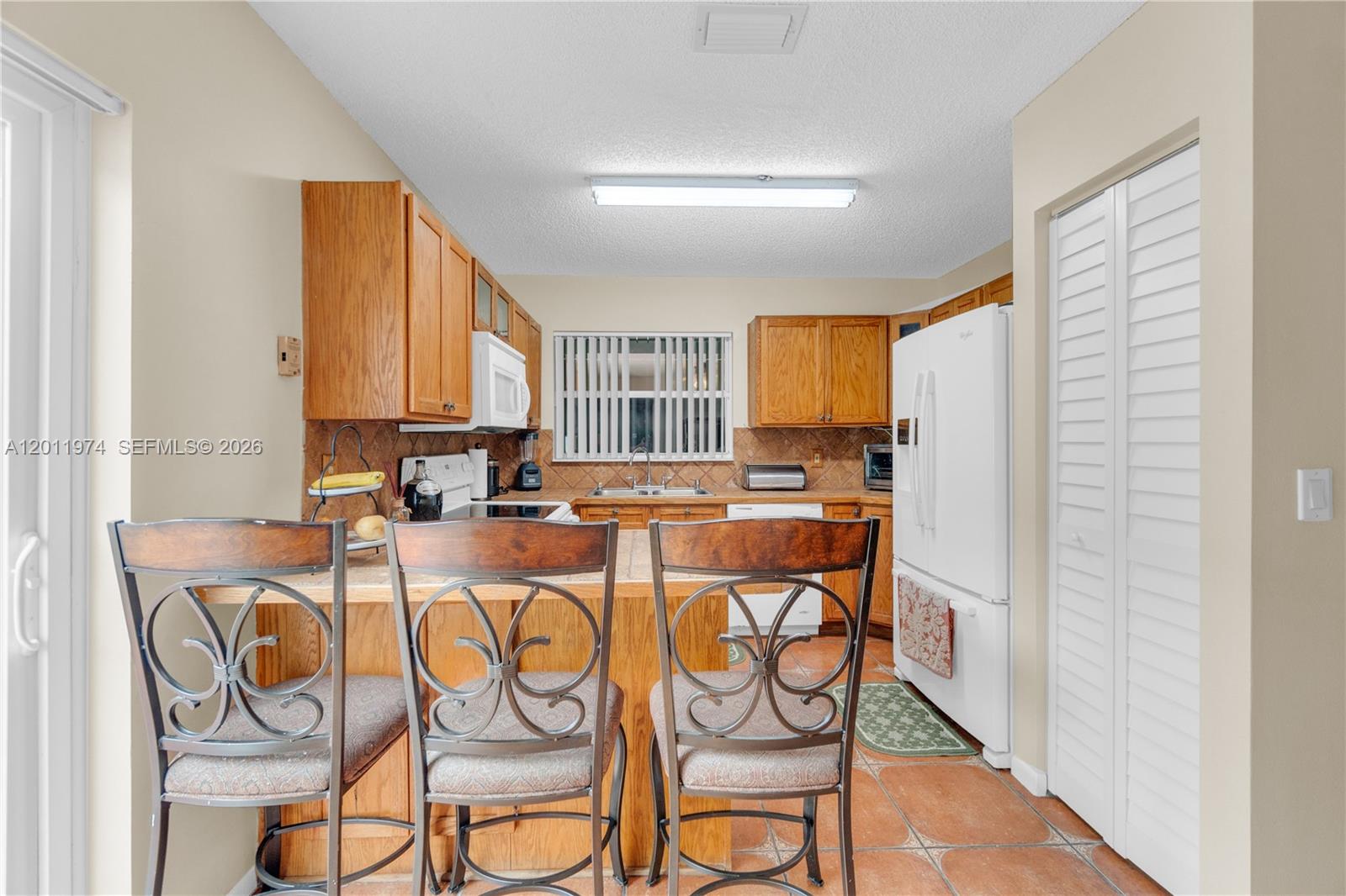 A kitchen features wood cabinets, a breakfast bar with three chairs, and terracotta tile flooring — 375 W Riverbend Dr, Sunrise FL 33326, SUNRISE, FL