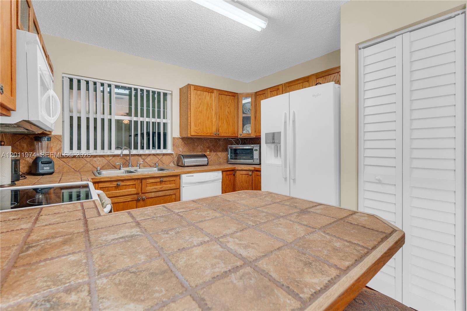 A kitchen features wood cabinets, tile countertops, white appliances, and a tiled backsplash — 375 W Riverbend Dr, Sunrise FL 33326, SUNRISE, FL