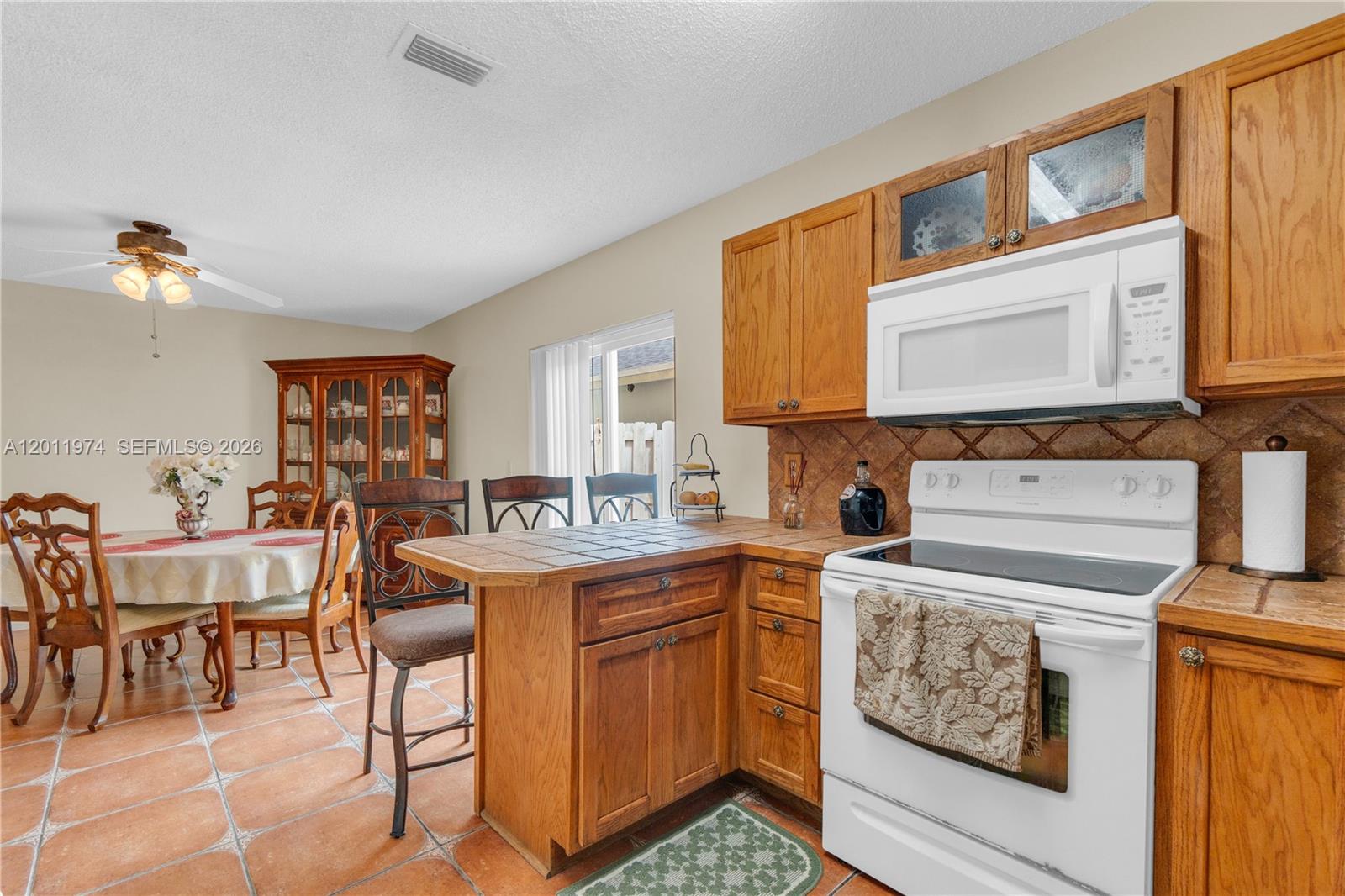 A kitchen with oak cabinets, tile countertops, and a dining area with a wooden hutch — 375 W Riverbend Dr, Sunrise FL 33326, SUNRISE, FL