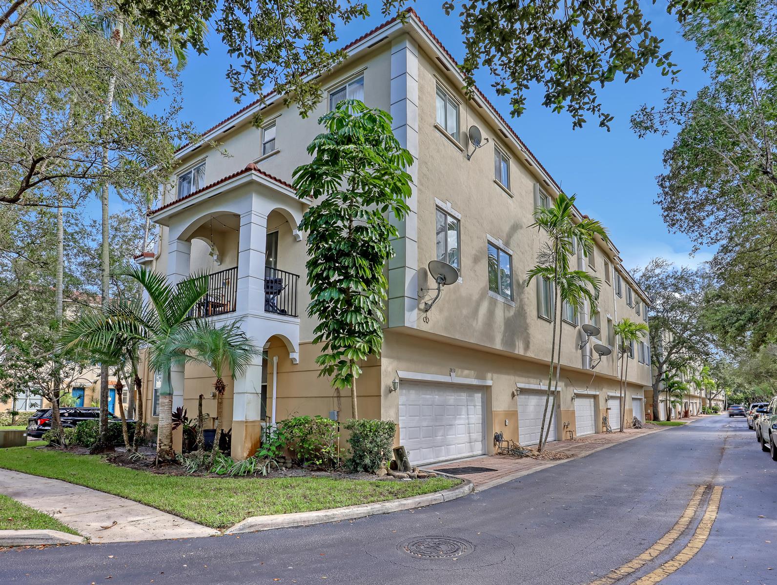 A three-story beige townhouse with a balcony, multiple garage doors, and surrounding palm trees — 2850 S Oasis Drive, Boynton Beach FL 33426, BOYNTON BEACH, FL