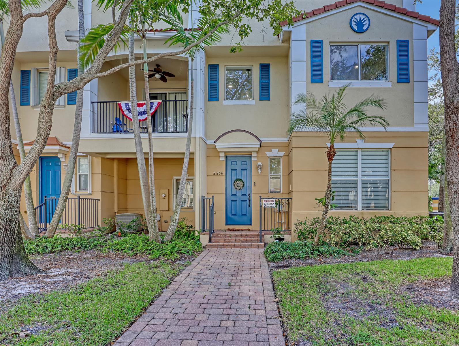 A two-story townhouse exterior features a blue front door, a brick walkway, and palm trees — 2850 S Oasis Drive, Boynton Beach FL 33426, BOYNTON BEACH, FL