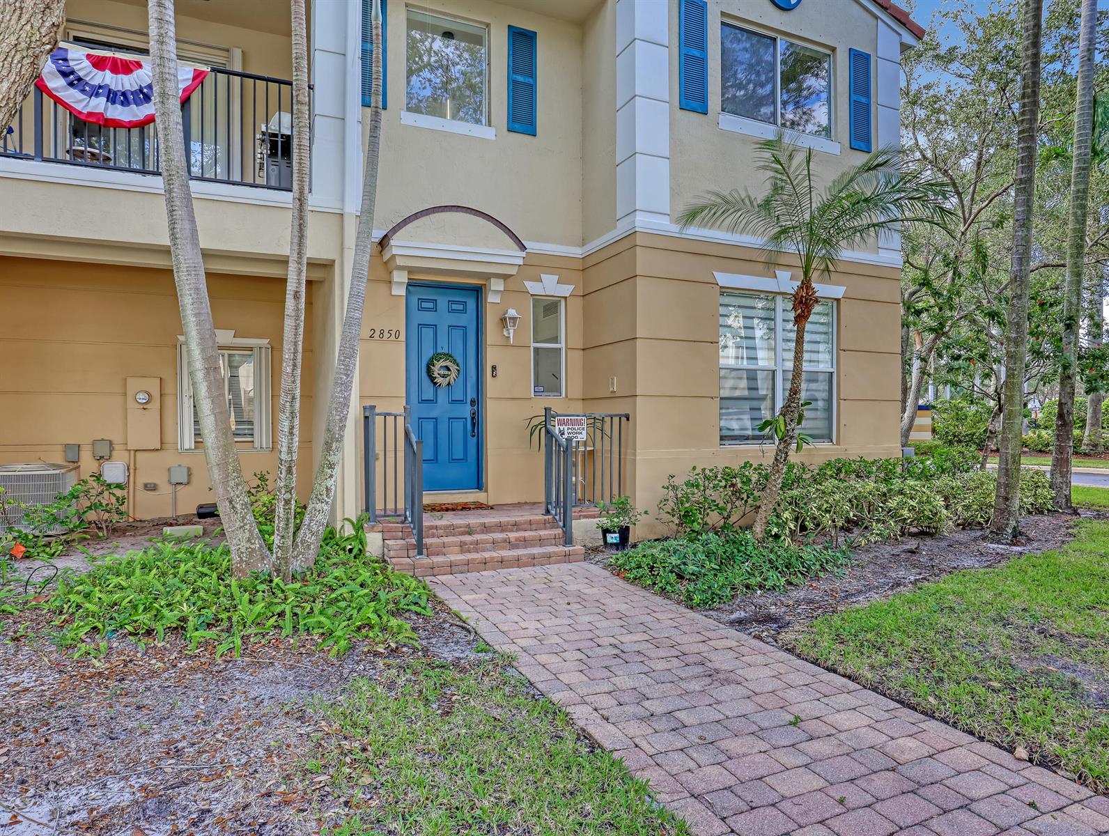A two-story tan townhouse with a blue front door, brick walkway, and palm trees — 2850 S Oasis Drive, Boynton Beach FL 33426, BOYNTON BEACH, FL