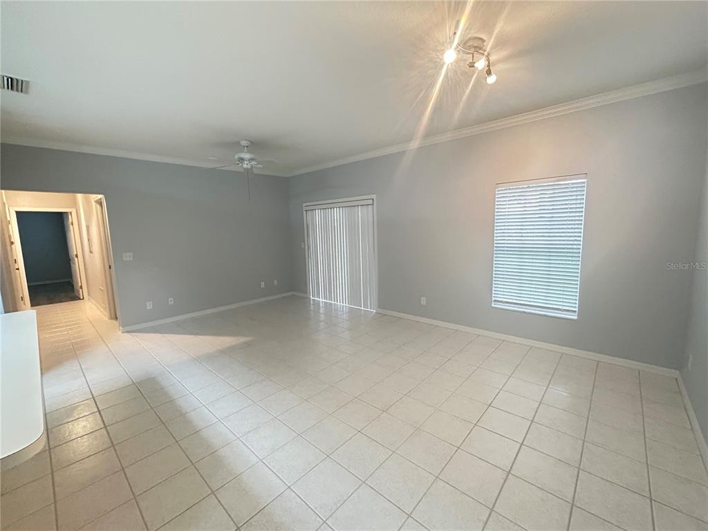 An empty living room features light gray walls, white tile flooring, and a sliding glass door — 1202 EAGLE POND DRIVE UNIT 1202, WINTER HAVEN, FL