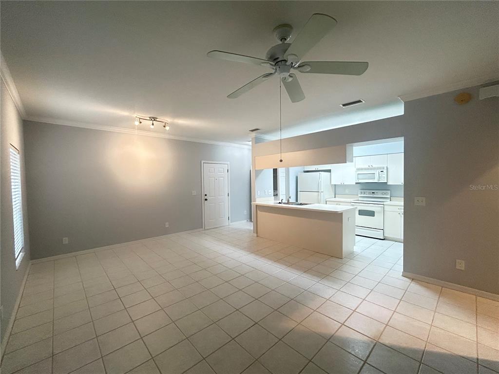 An open-concept living and dining area features white tile flooring, a ceiling fan, and kitchen — 1202 EAGLE POND DRIVE UNIT 1202, WINTER HAVEN, FL